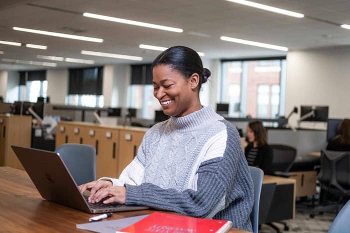 Lady smiling typing at a laptop on a desk.